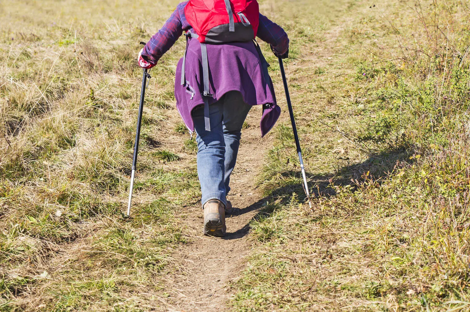 A woman hiking up a dirt trail through dry mountain grass