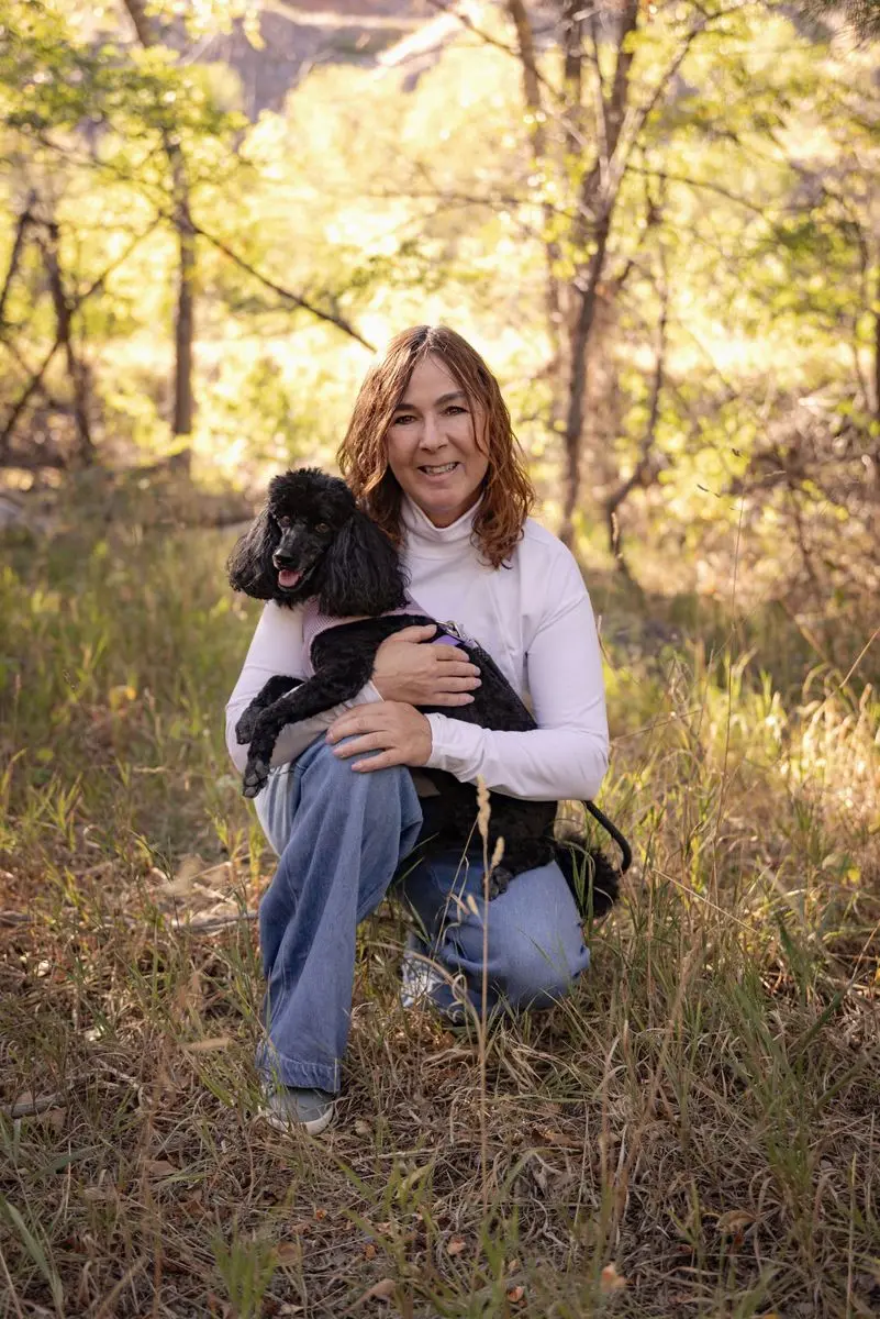 Melissa Hunt kneeling in a mountain meadow with her poodle, Bree